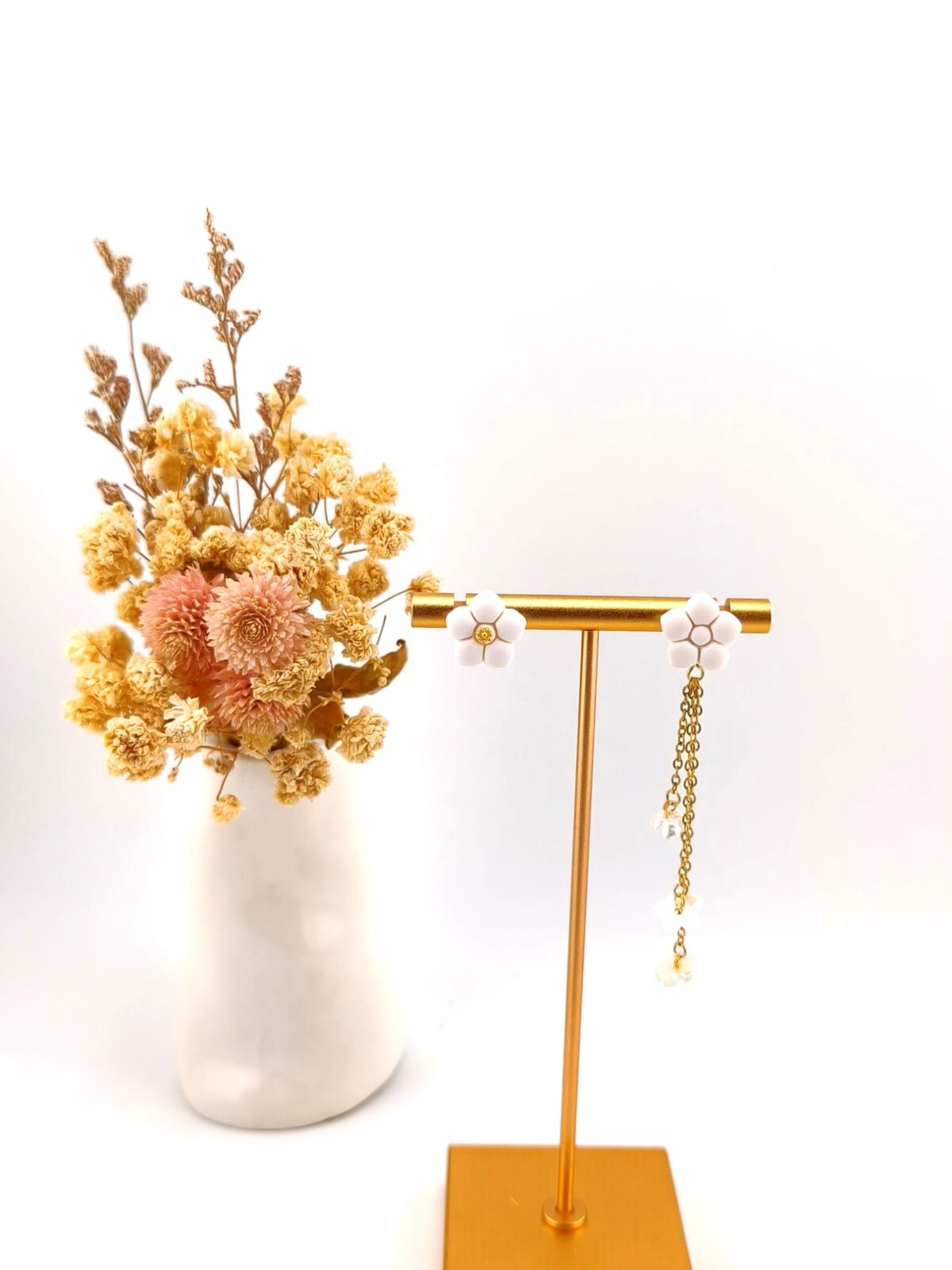 Brincos desemparelhados com flores brancas e detalhes dourados em expositor